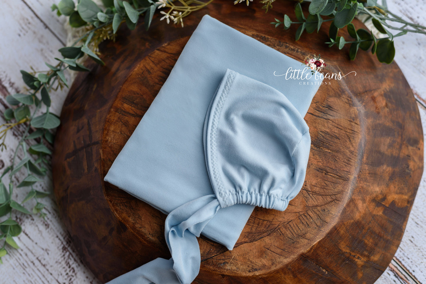 Flat lay of blue newborn photography prop set, featuring a stretch fabric bonnet and wrap for professional newborn photo sessions.