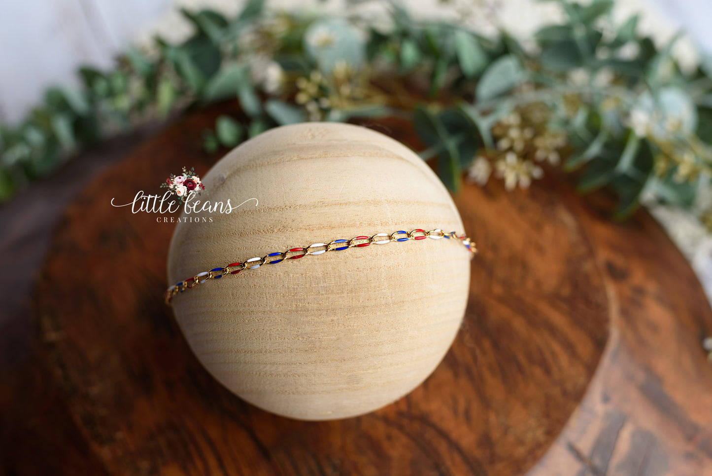 Handcrafted red, white, and blue newborn tieback headband displayed on a wooden prop with greenery background – perfect for baby photoshoots and patriotic themes.