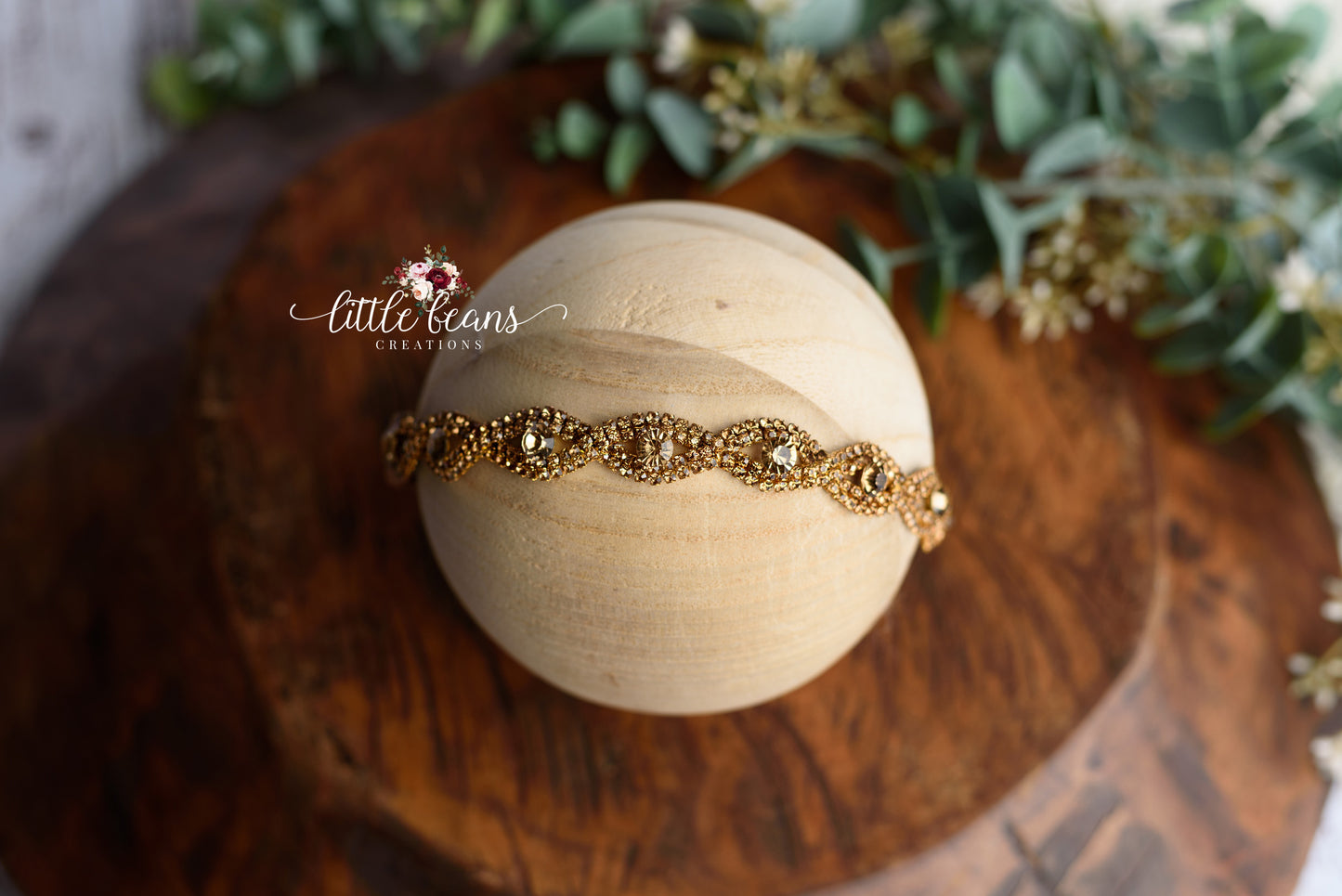 Bronzed Amber newborn tieback headband with gold crystal detailing on wooden styling sphere.
